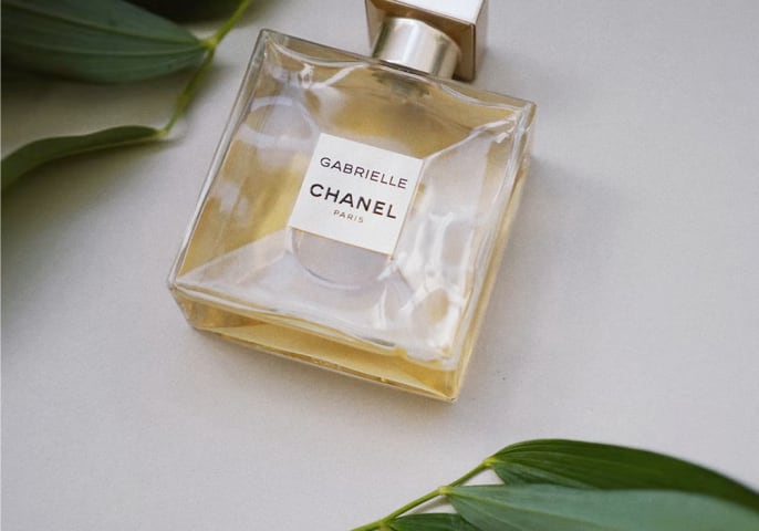 Gabrielle Perfume lying on a table with few leaves on top and bottom